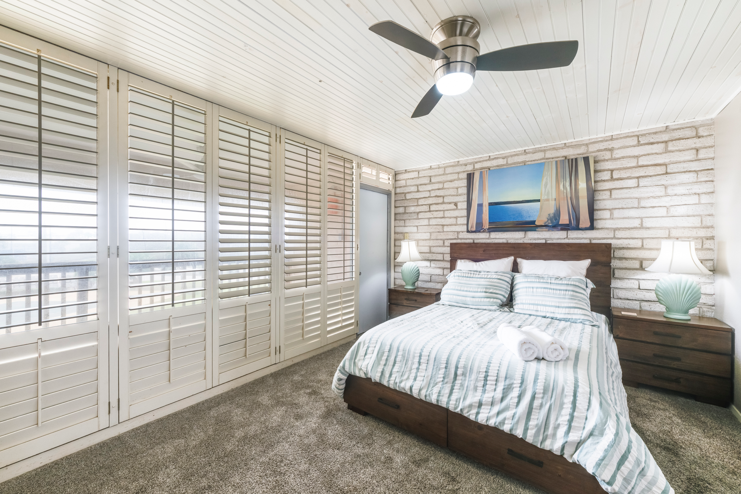 Bright primary bedroom with striped bedding, lamps, and large windows in Port Aransas condo