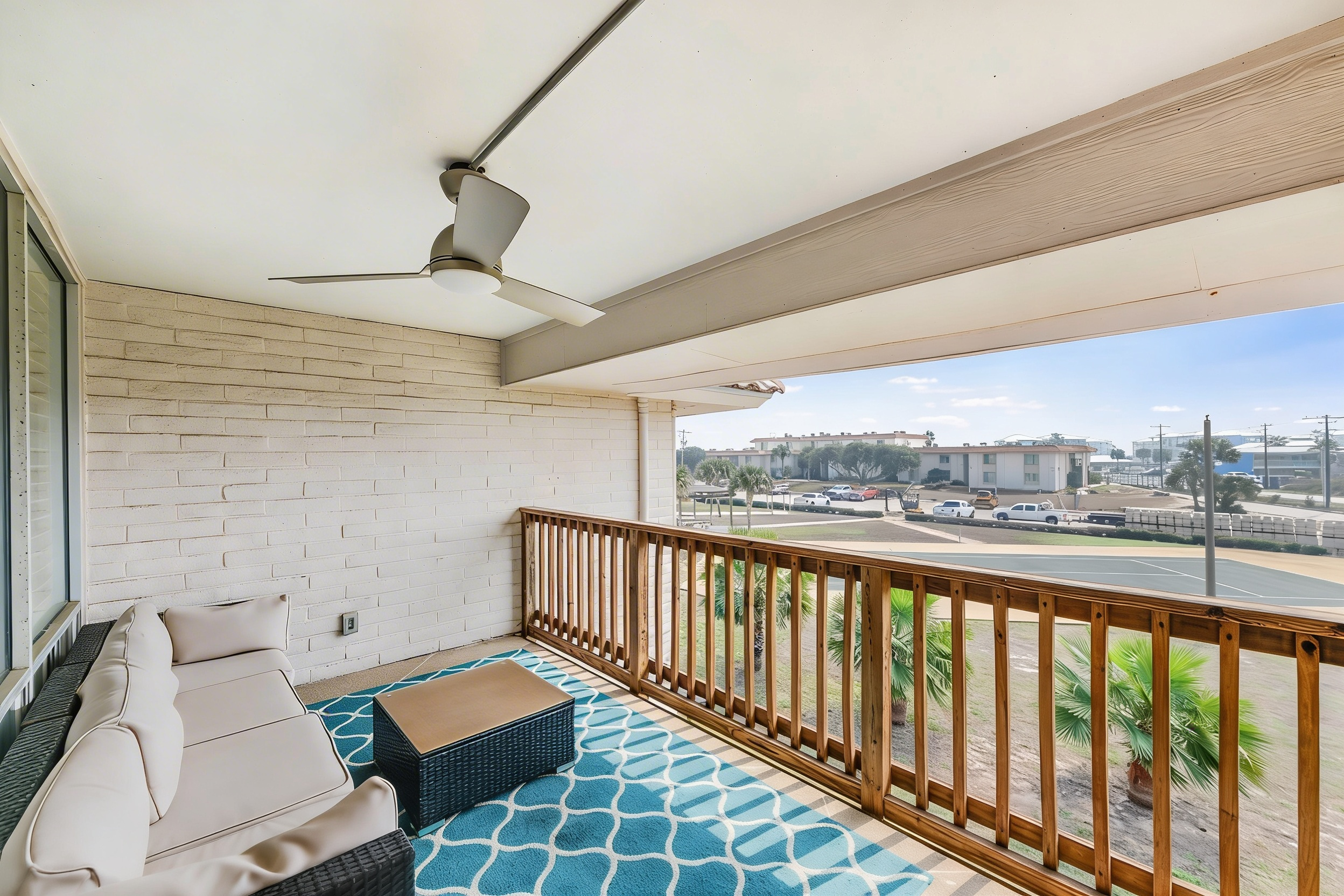 Covered balcony off upstairs bedroom with sectional seating overlooking pool and palms