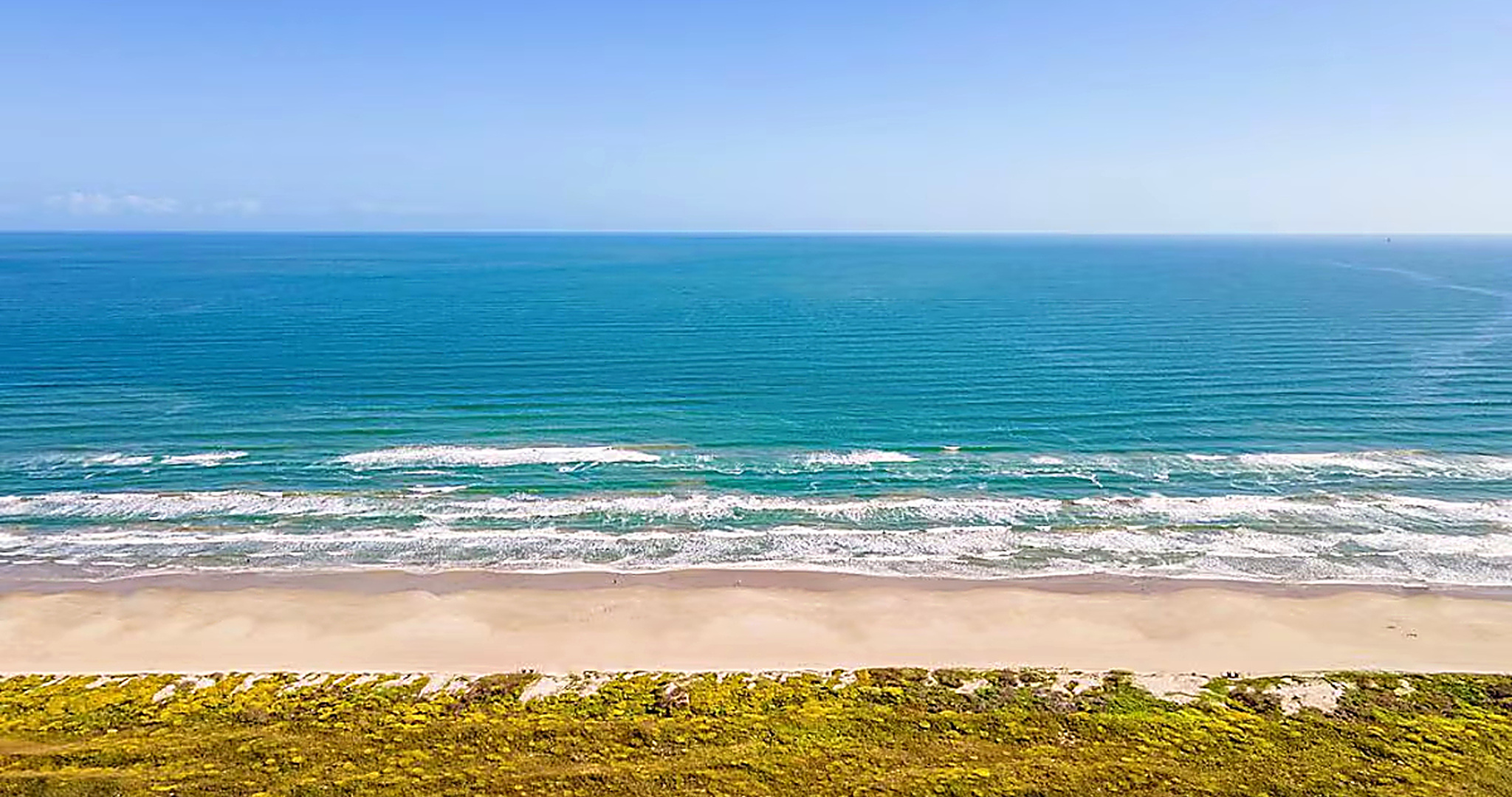 Wide sandy Port Aransas beach with gentle Gulf waves and natural dune vegetation