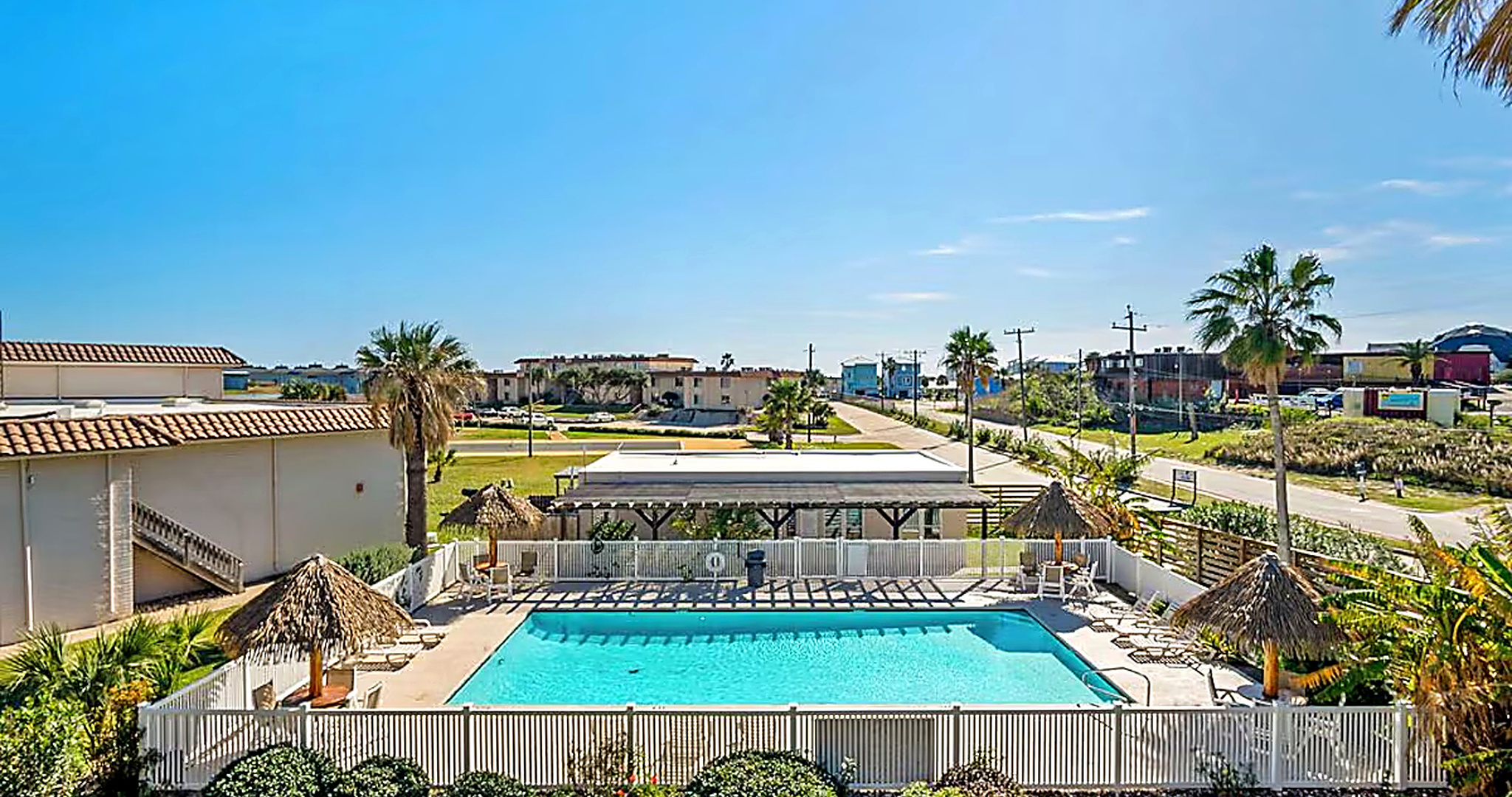 Sunny Port Aransas condo pool with thatched palapa umbrellas and palm trees