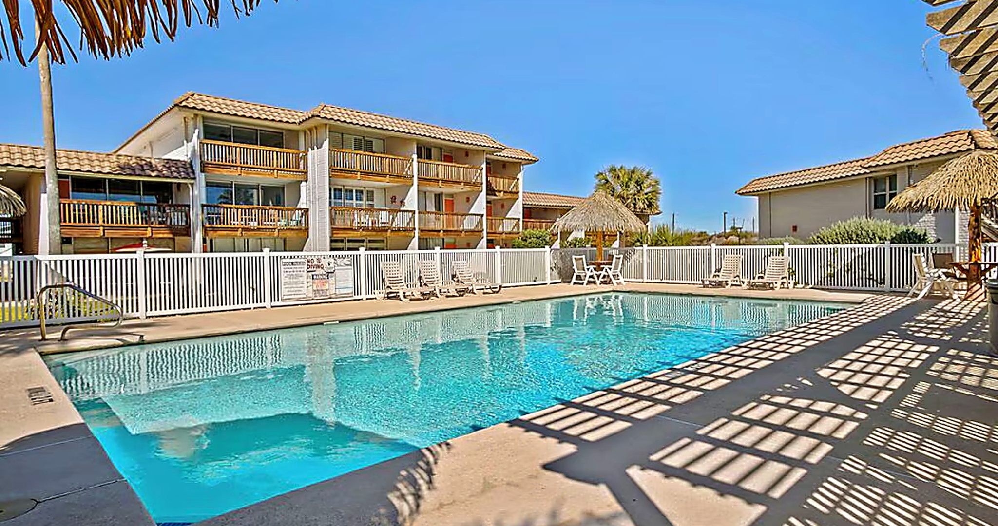 Sunny Port Aransas condo pool with thatched palapa umbrellas and palm trees