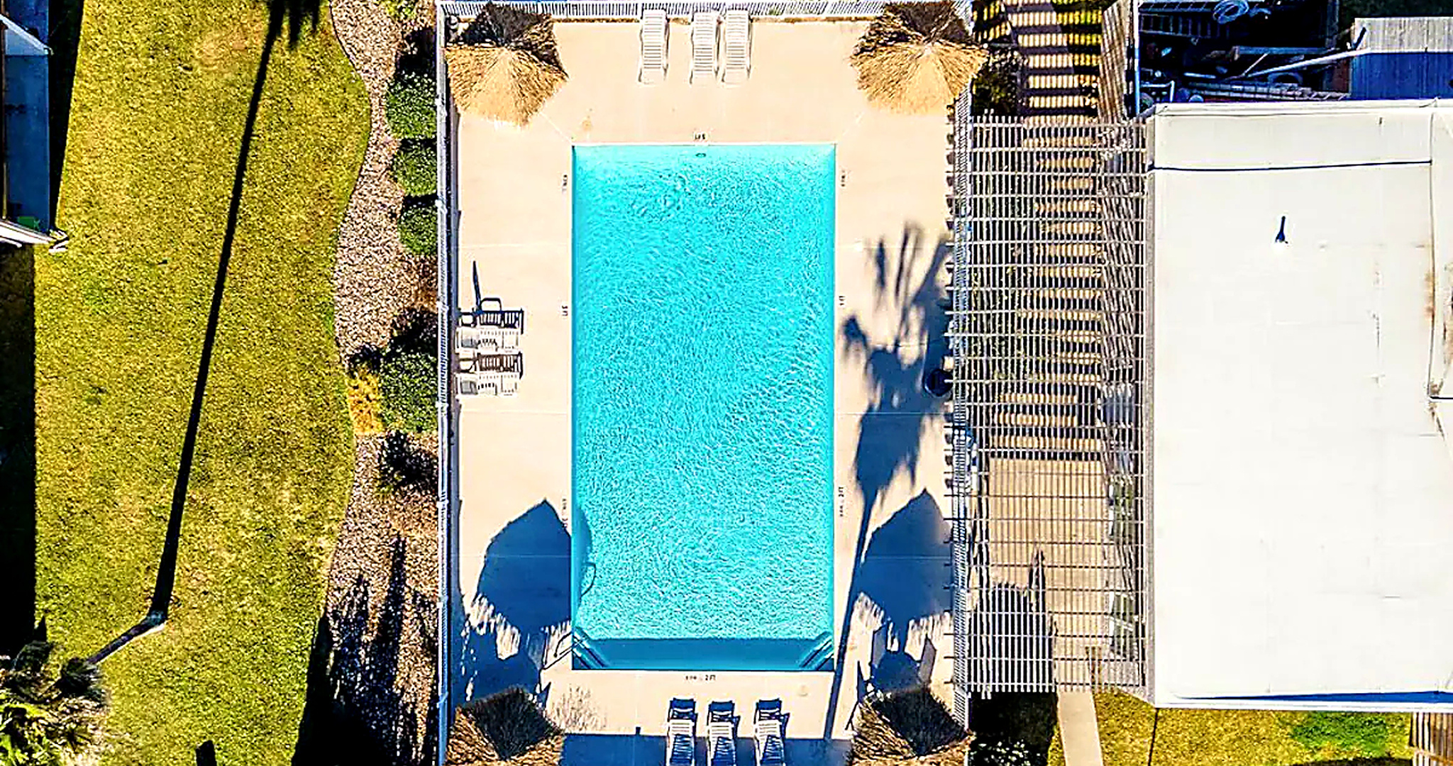 Aerial view of rectangular condo pool with palapa umbrellas, lounge chairs, and lawn