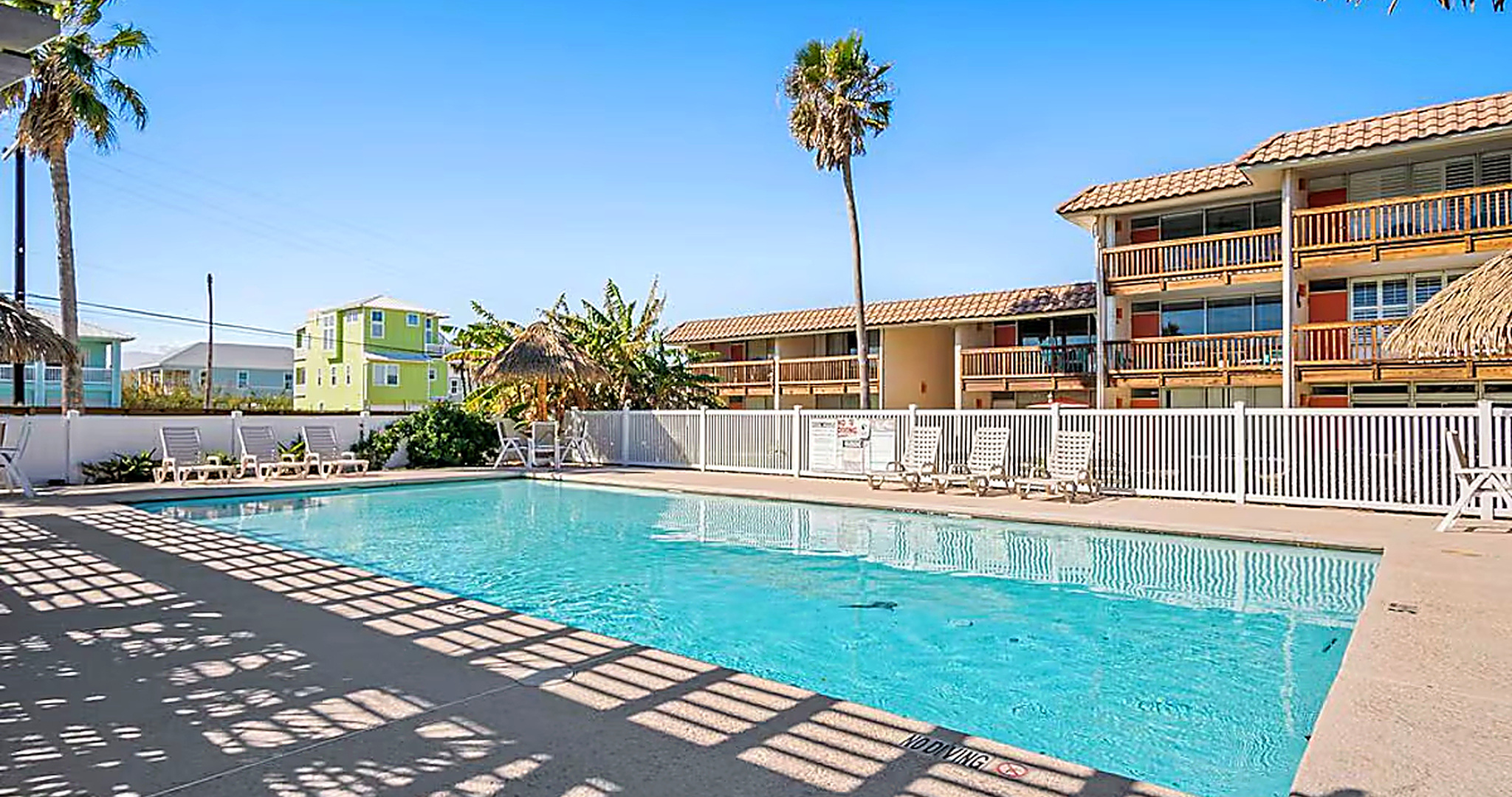 Sunny Port Aransas condo pool with thatched palapa umbrellas and palm trees